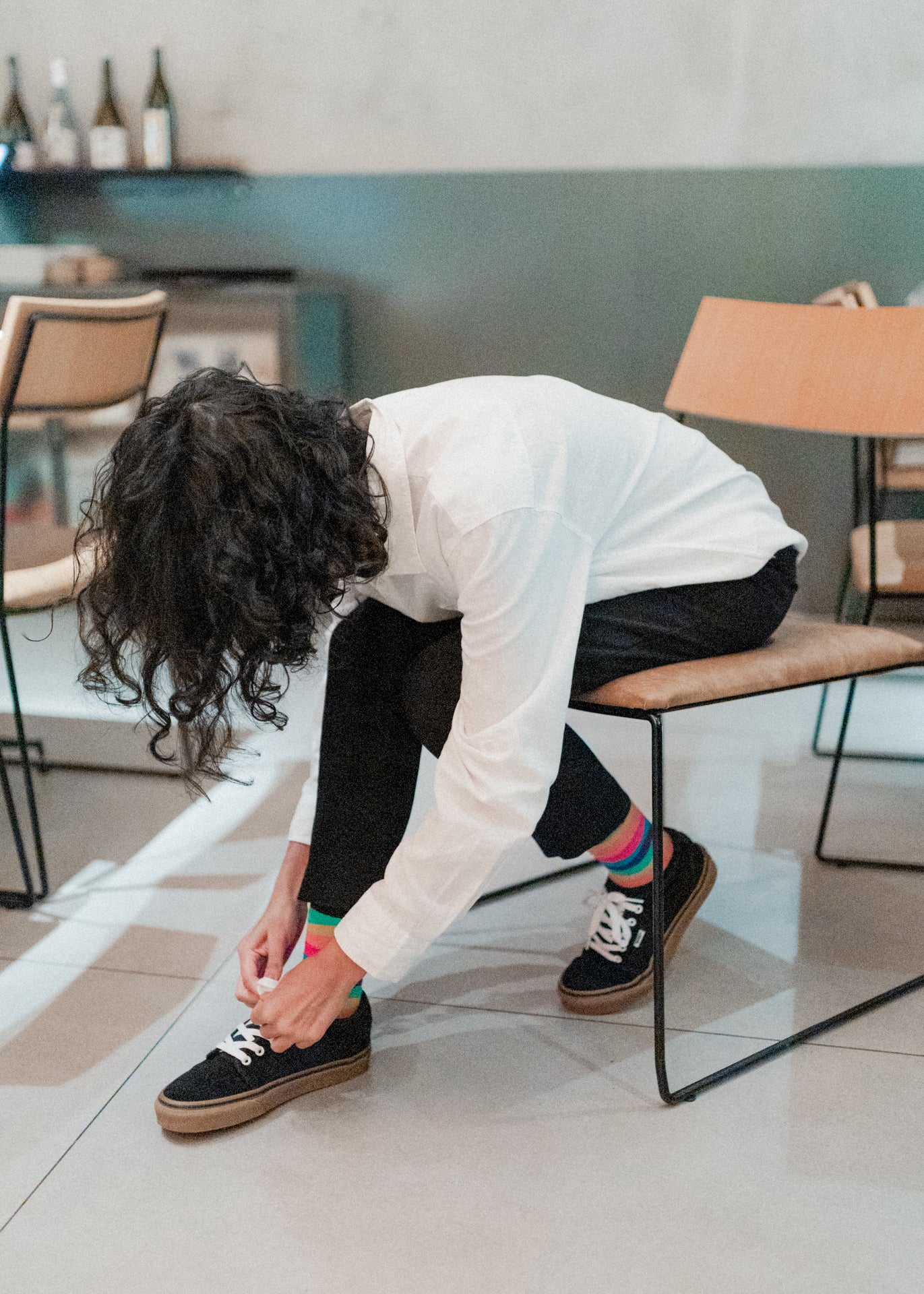 Person adjusting their black Vans sneakers with colorful socks in a casual setting.